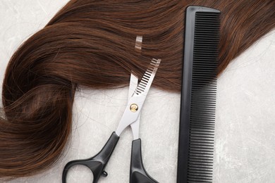 Brown hair strand, comb and professional scissors on grey table, top view