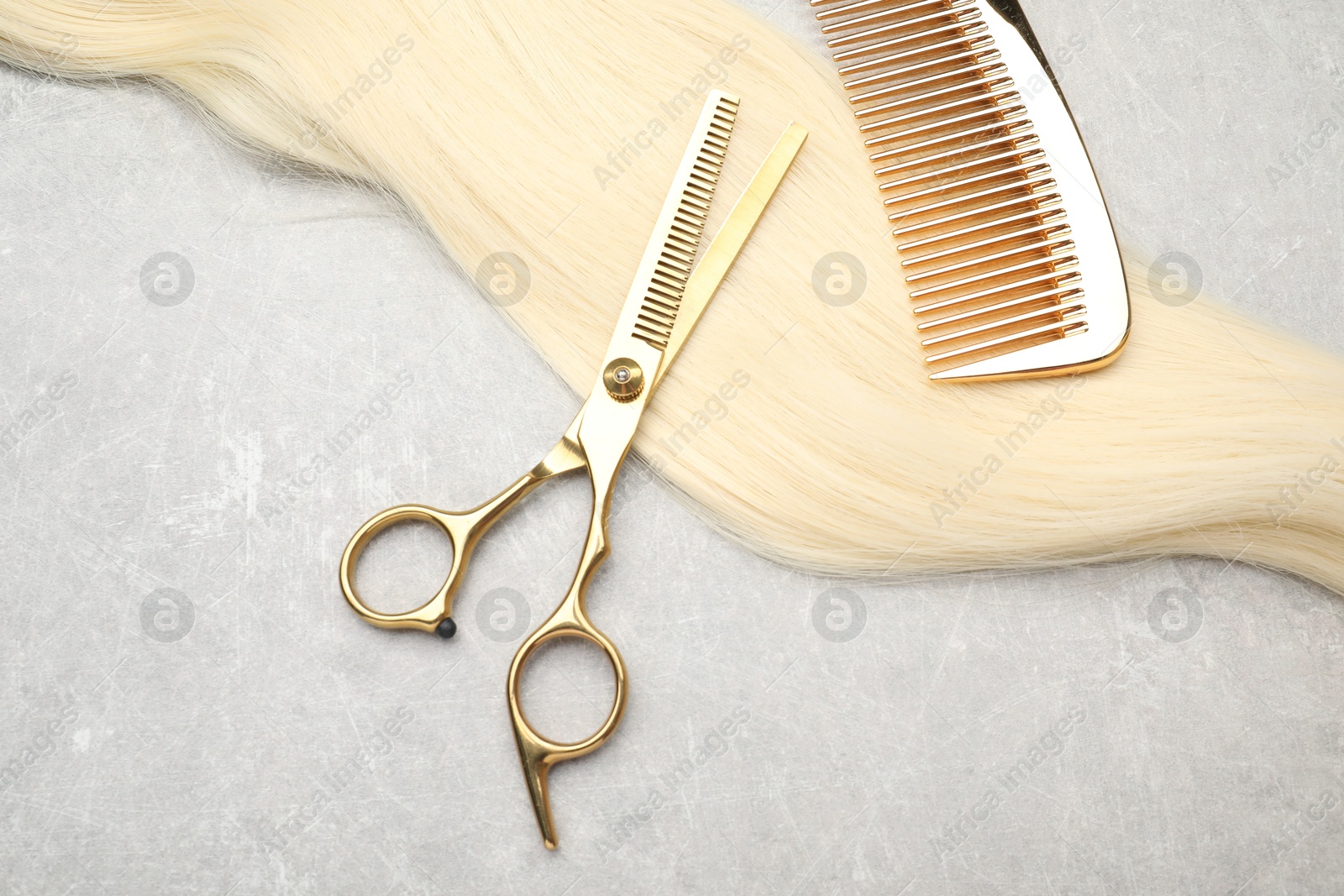 Photo of Blonde hair strand, comb and professional scissors on grey table, above view