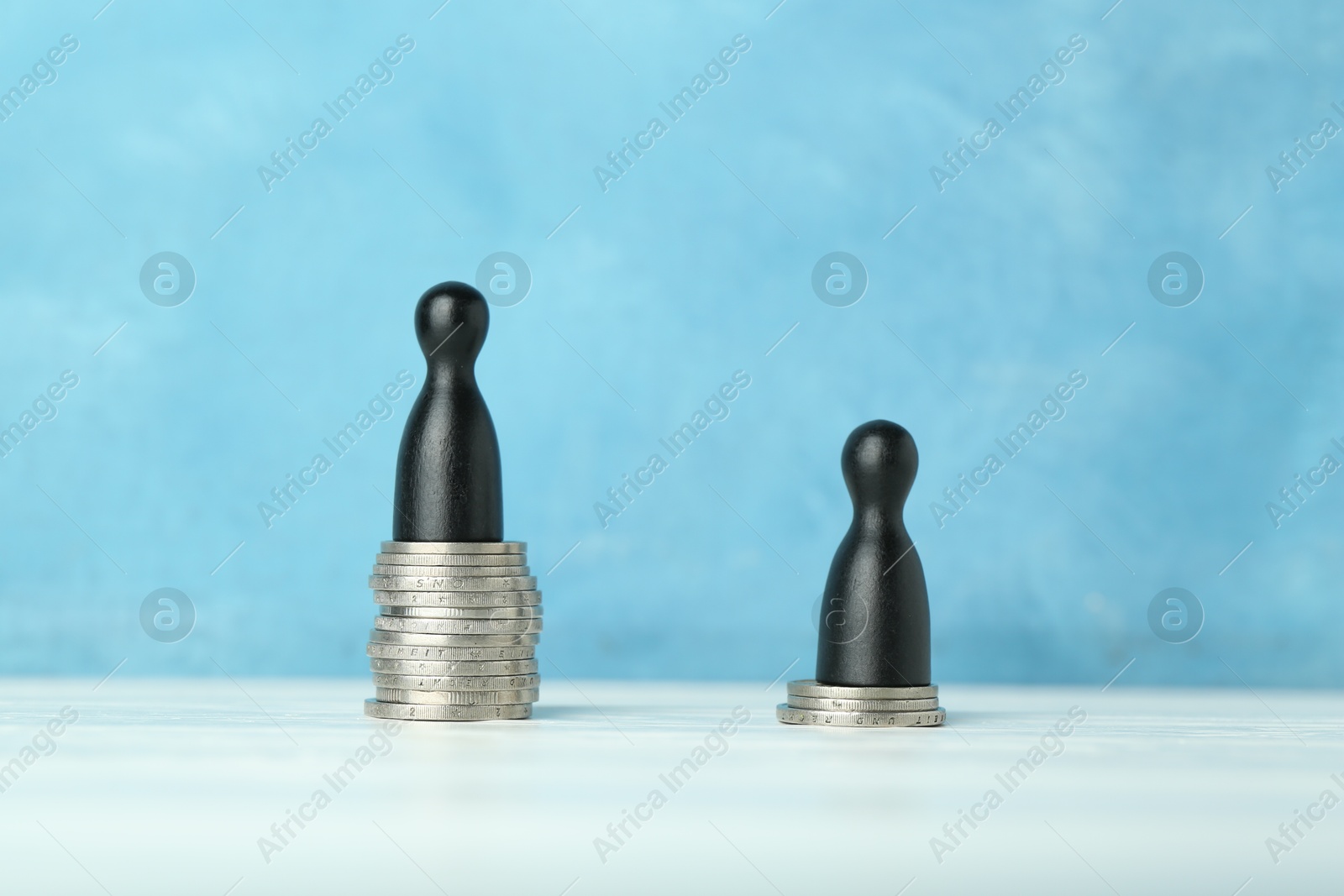 Photo of Financial inequality. One wooden figure on bigger stack of coins than another on white table