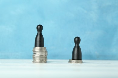 Financial inequality. One wooden figure on bigger stack of coins than another on white table