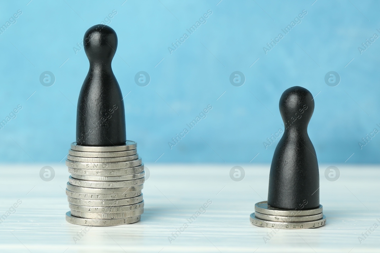 Photo of Financial inequality. One wooden figure on bigger stack of coins than another on white table