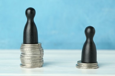 Photo of Financial inequality. One wooden figure on bigger stack of coins than another on white table