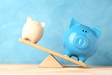 Financial inequality. Bigger piggy bank overweighting smaller one on scales against light blue background