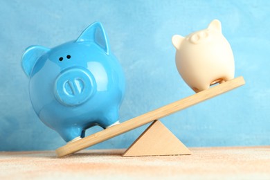 Photo of Financial inequality. Piggy banks of different size showing imbalance on scales against light blue background