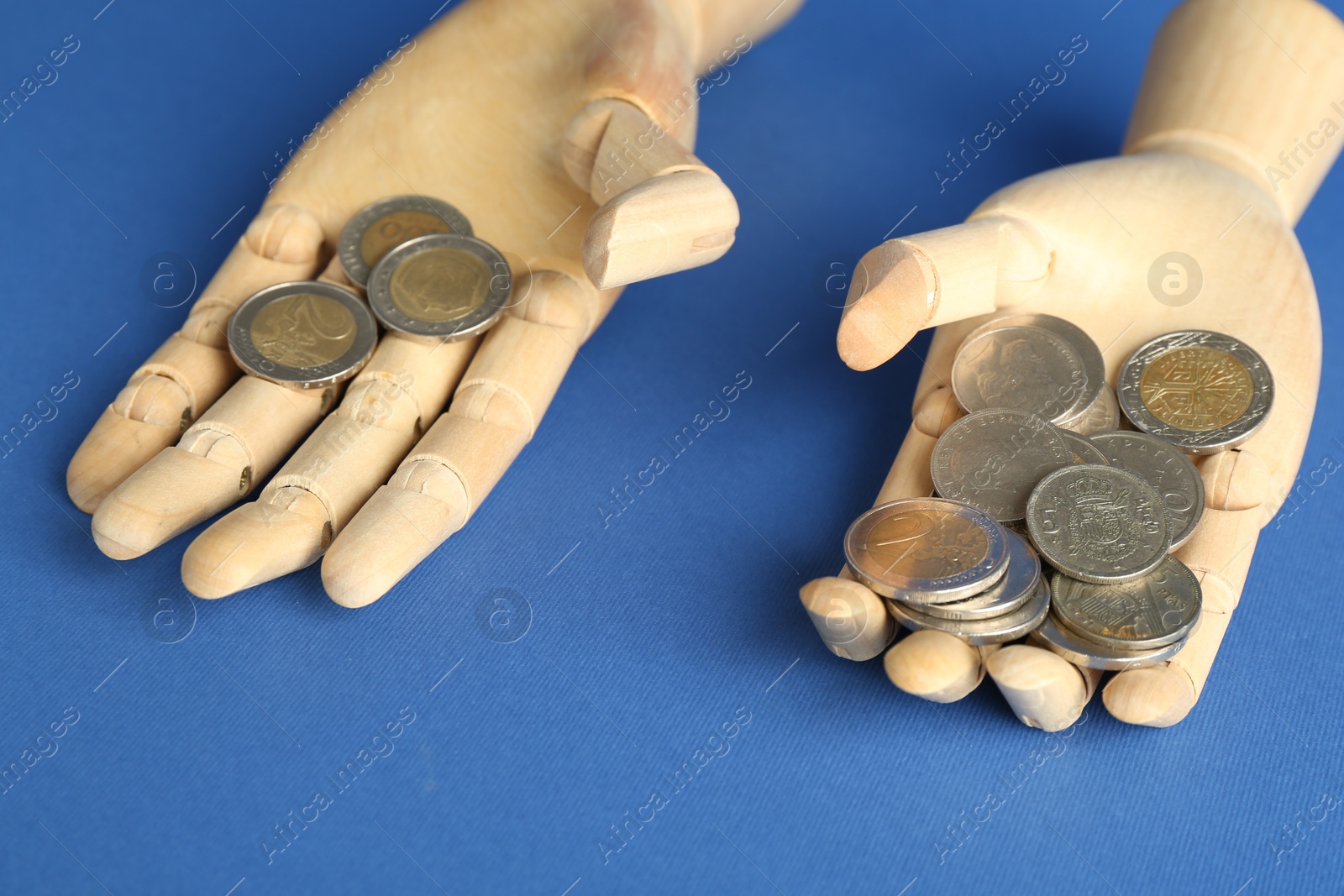 Photo of Financial inequality. Uneven amount of coins in mannequin hands on blue background