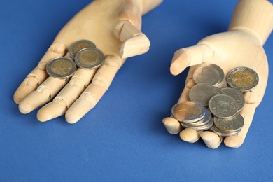 Photo of Financial inequality. Uneven amount of coins in mannequin hands on blue background