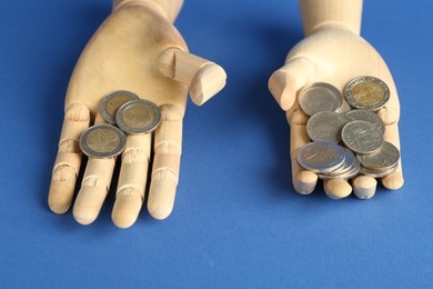 Photo of Financial inequality. Uneven amount of coins in mannequin hands on blue background