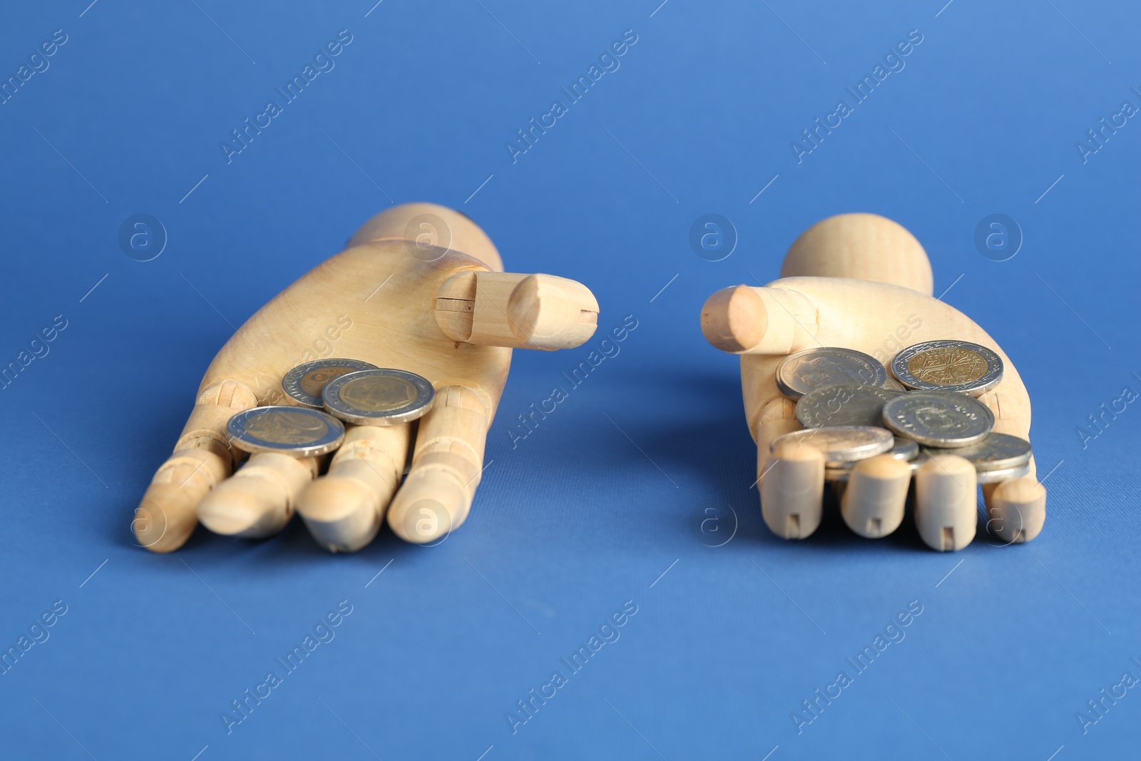 Photo of Financial inequality. Uneven amount of coins in mannequin hands on blue background