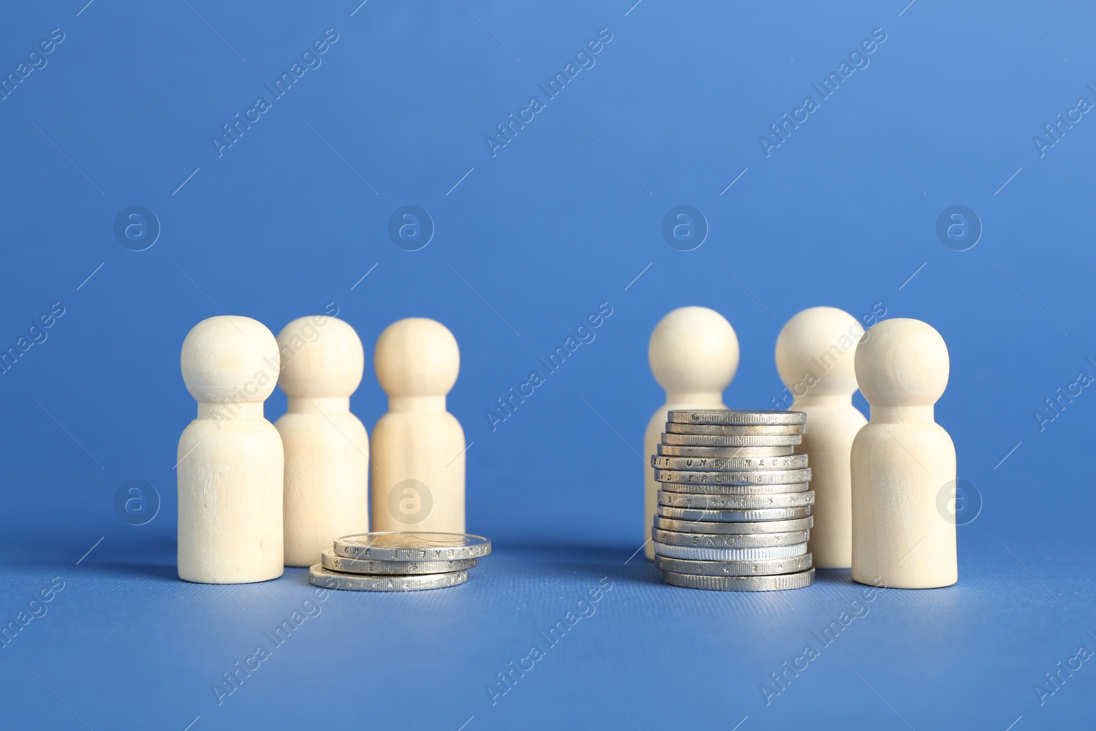 Photo of Financial inequality. Wooden figures and stacked coins of different height against blue background