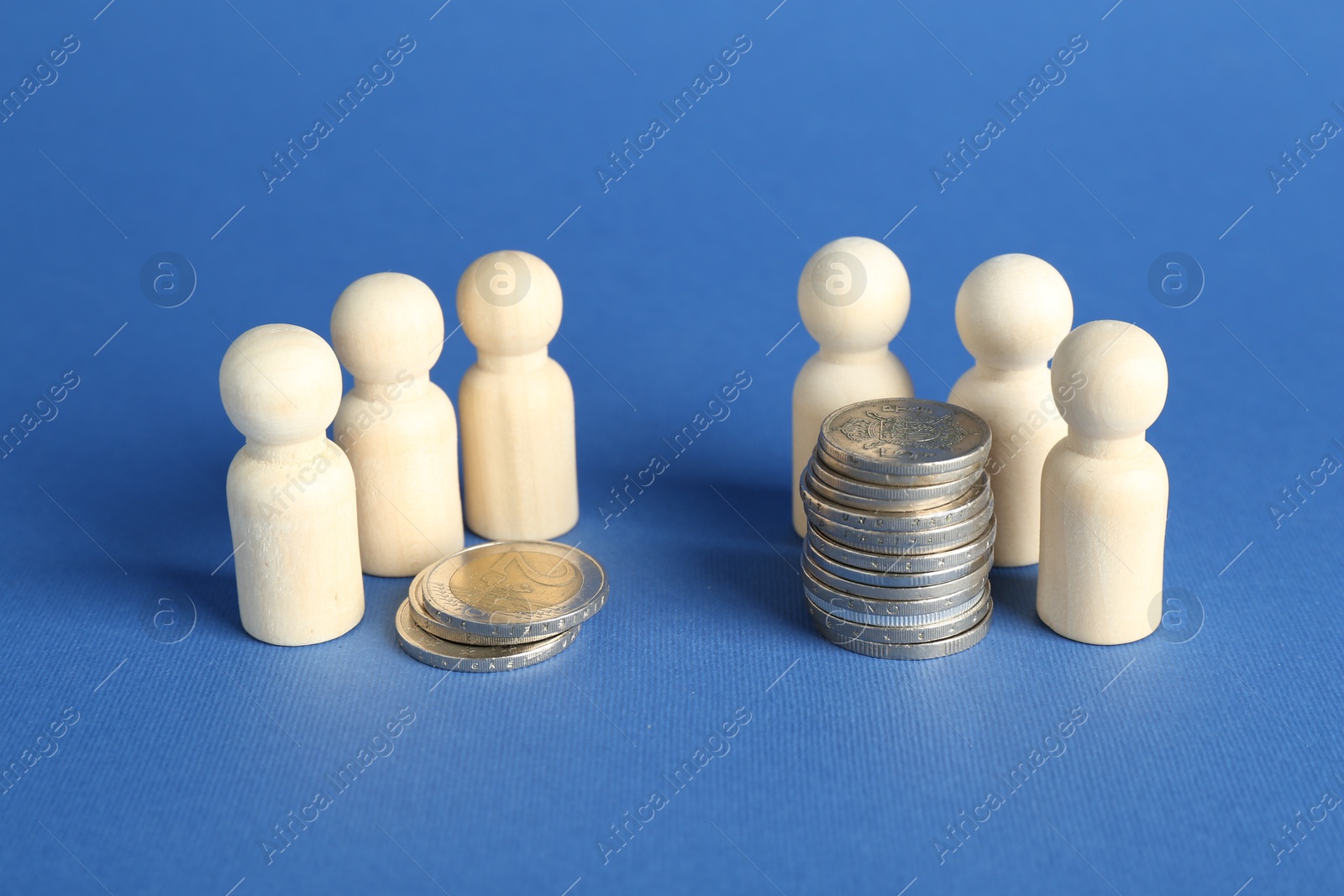 Photo of Financial inequality. Wooden figures and stacked coins of different height against blue background