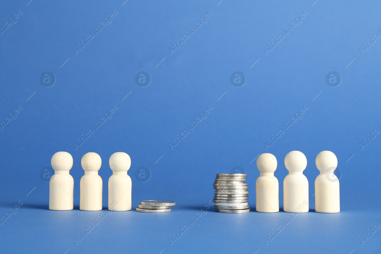 Photo of Financial inequality. Wooden figures and stacked coins of different height against blue background