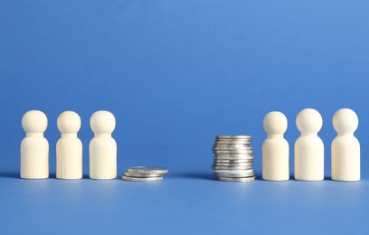 Photo of Financial inequality. Wooden figures and stacked coins of different height against blue background