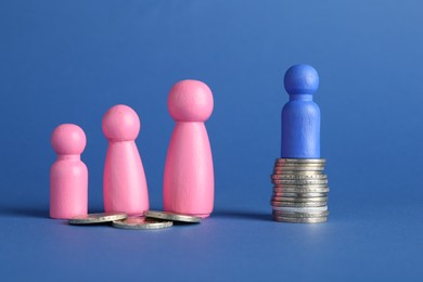 Photo of Financial inequality. Male and female figures with uneven amount of coins on blue background