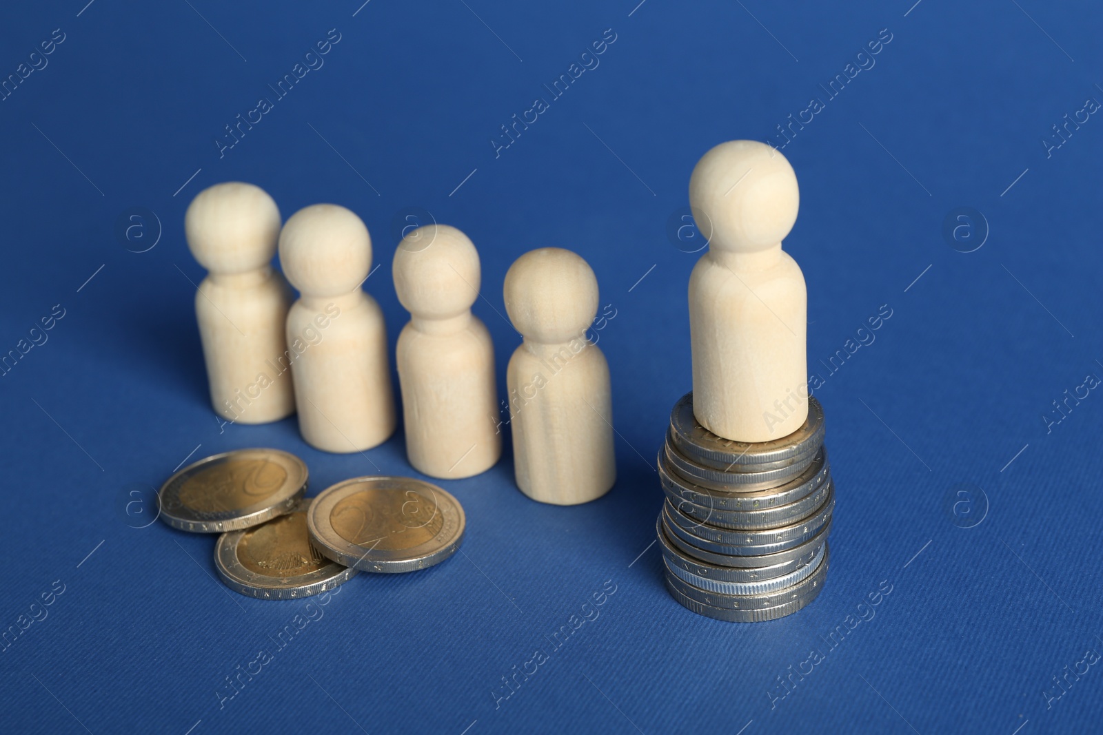 Photo of Financial inequality. Wooden figures with uneven amount of coins on blue background