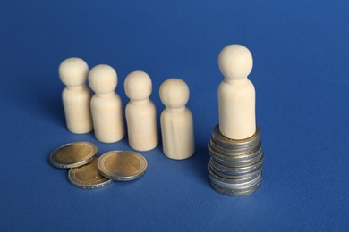 Photo of Financial inequality. Wooden figures with uneven amount of coins on blue background