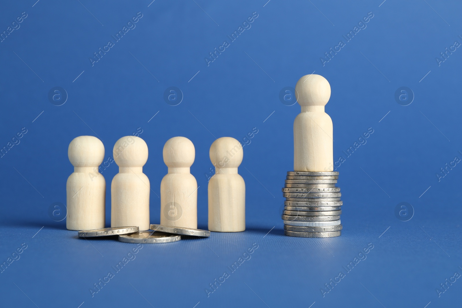 Photo of Financial inequality. Wooden figures with uneven amount of coins on blue background