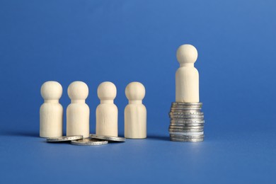 Photo of Financial inequality. Wooden figures with uneven amount of coins on blue background