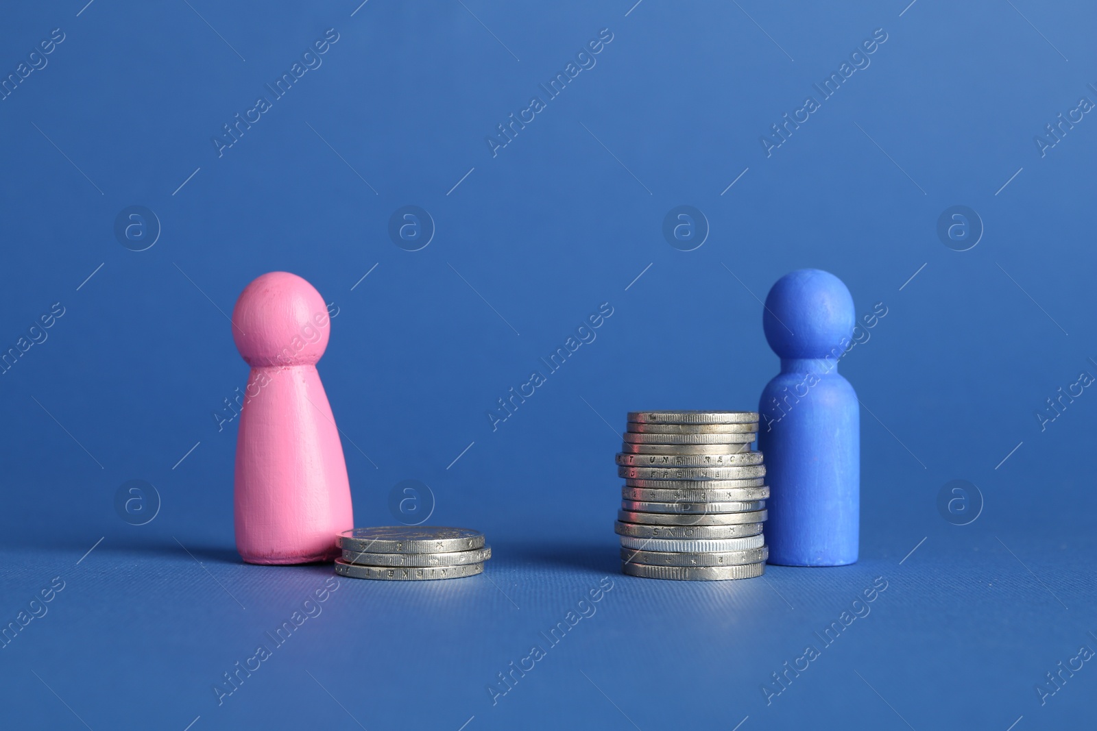 Photo of Financial inequality. Male and female figures on stacked coins of different height against blue background