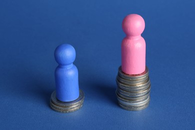 Financial inequality. Male and female figures on stacked coins of different height against blue background