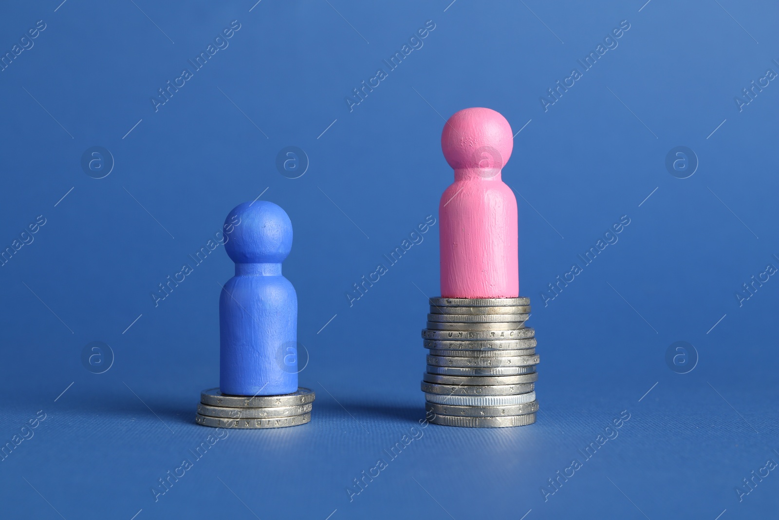 Photo of Financial inequality. Male and female figures on stacked coins of different height against blue background