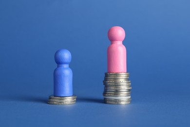 Financial inequality. Male and female figures on stacked coins of different height against blue background