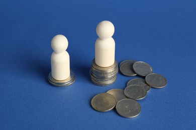 Photo of Financial inequality. Wooden figures with uneven amount of coins on blue background