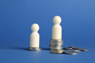 Photo of Financial inequality. Wooden figures with uneven amount of coins on blue background