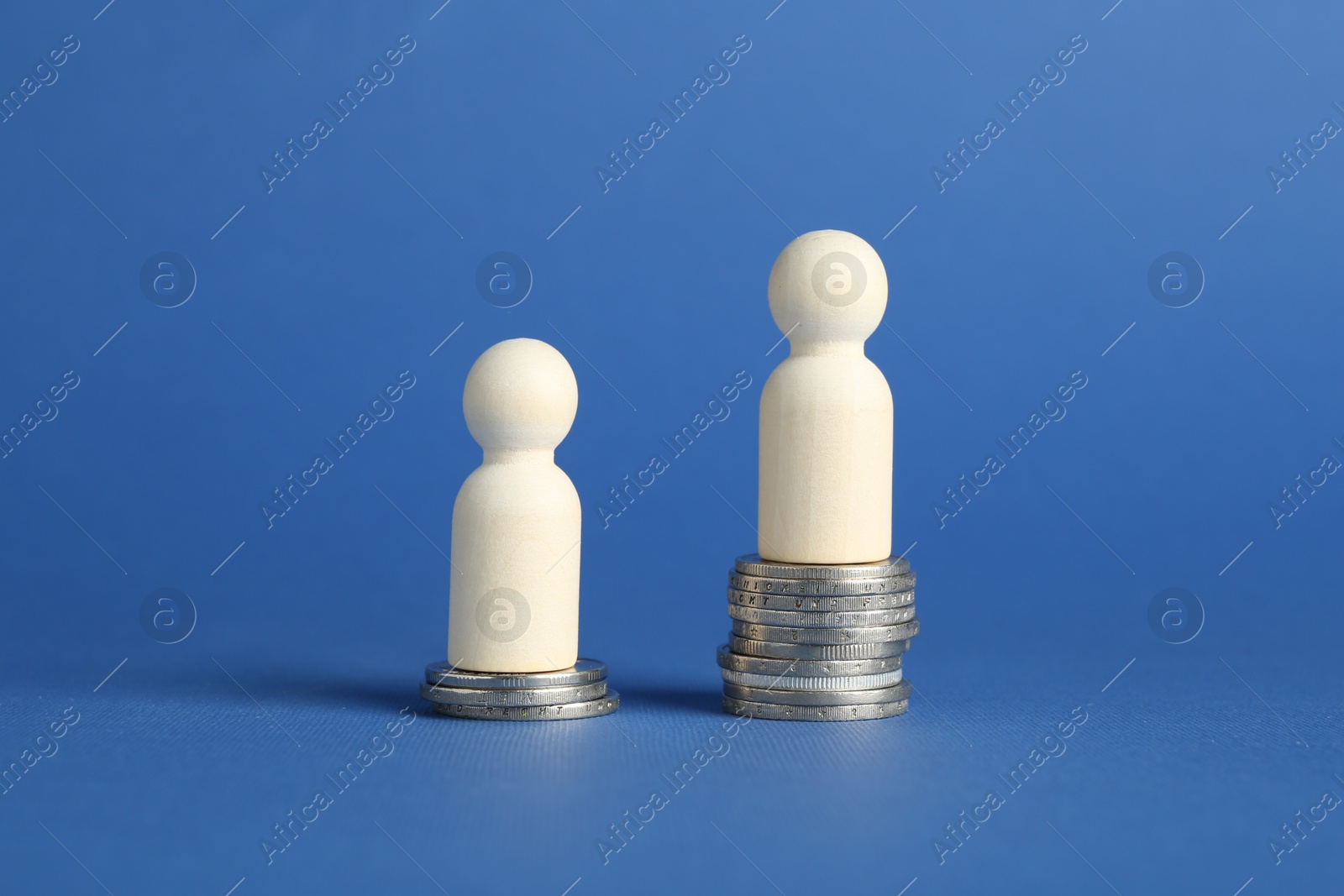 Photo of Financial inequality. Wooden figures on stacked coins of different height against blue background