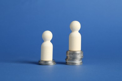 Financial inequality. Wooden figures on stacked coins of different height against blue background