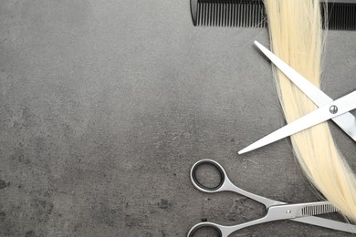 Blonde hair strand, comb and professional scissors on grey surface, flat lay. Space for text