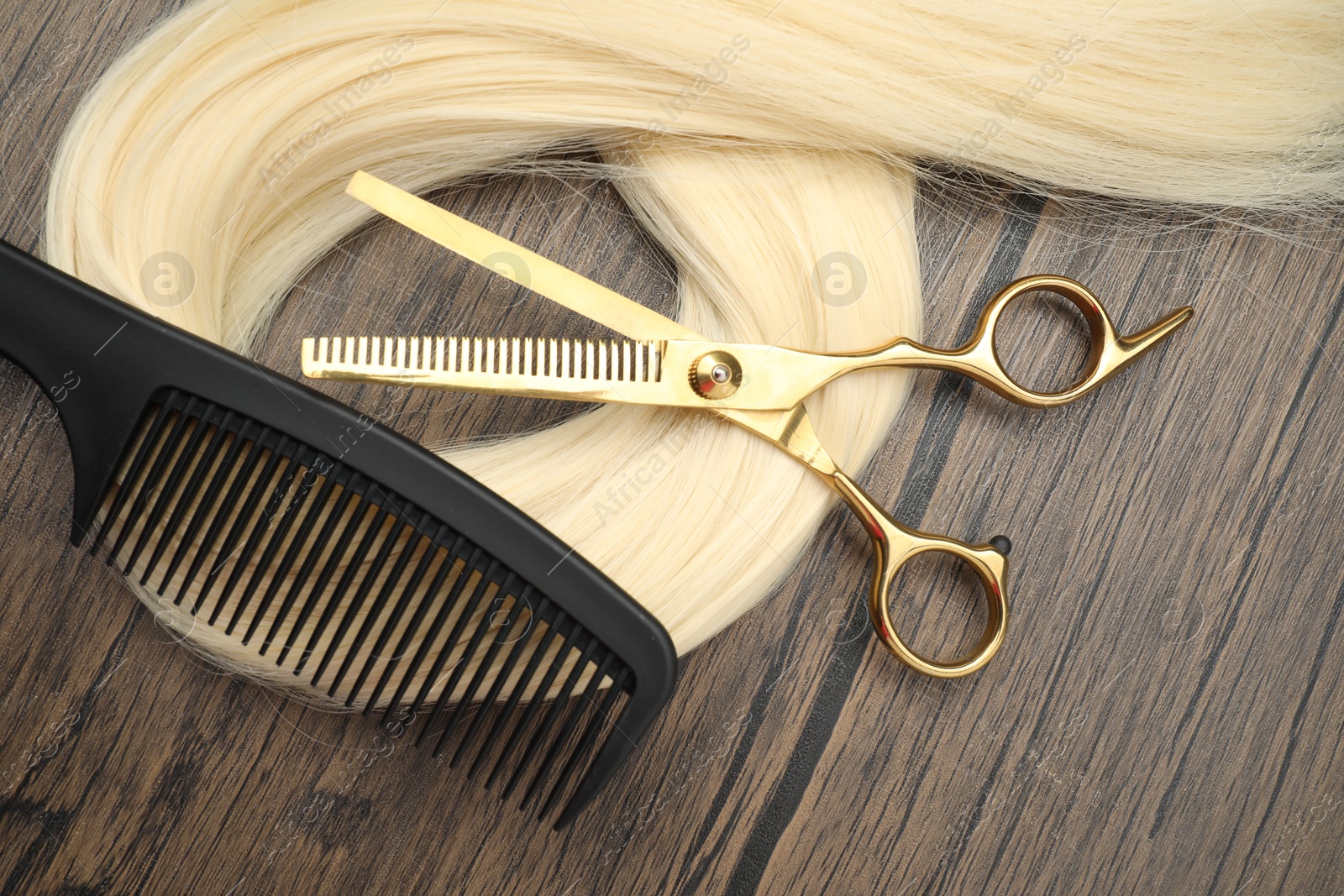 Photo of Blonde hair strand, comb and professional scissors on wooden surface, flat lay