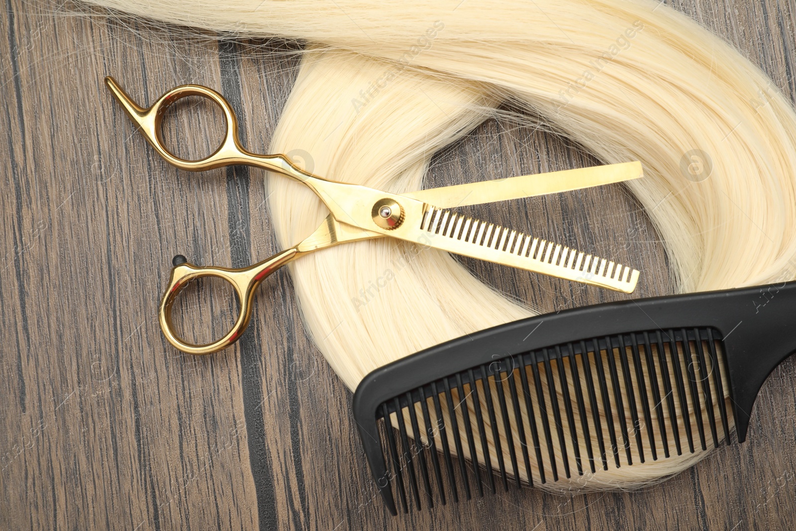 Photo of Blonde hair strand, comb and professional scissors on wooden surface, flat lay