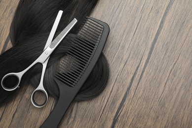 Photo of Black hair strand, comb and professional scissors on wooden surface, flat lay. Space for text