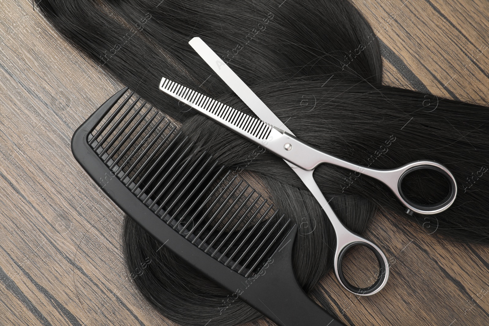 Photo of Black hair strand, comb and professional scissors on wooden surface, flat lay