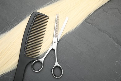 Blonde hair strand, comb and professional scissors on grey surface, flat lay. Space for text