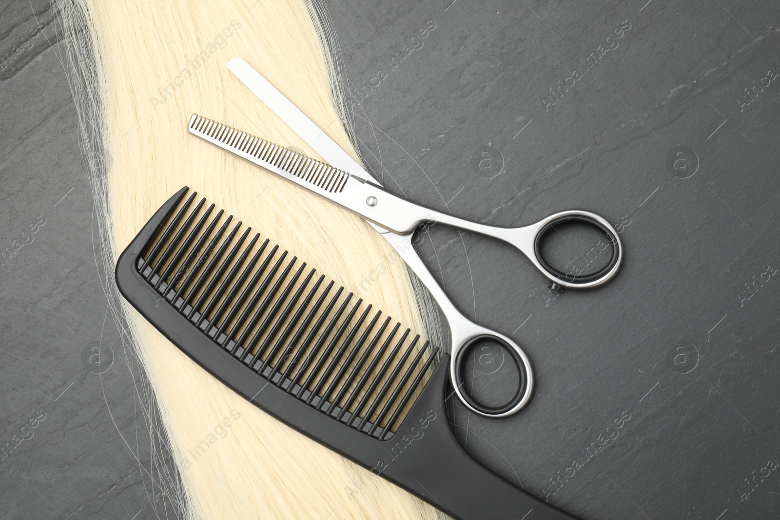 Photo of Blonde hair strand, comb and professional scissors on grey surface, flat lay