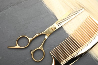 Photo of Blonde hair strand, comb and professional scissors on grey surface, flat lay