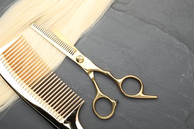 Blonde hair strand, comb and professional scissors on grey surface, flat lay