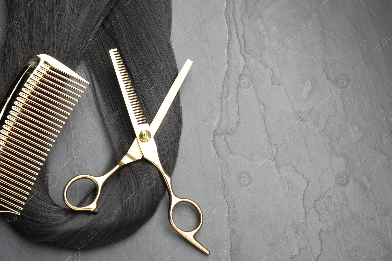 Photo of Black hair strand, comb and professional scissors on grey surface, flat lay. Space for text