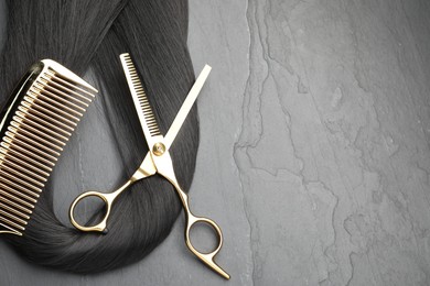 Photo of Black hair strand, comb and professional scissors on grey surface, flat lay. Space for text