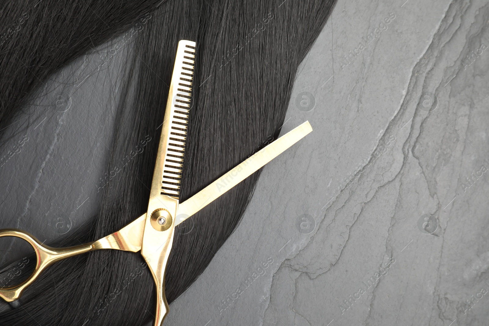 Photo of Black hair strand and professional scissors on grey surface, flat lay. Space for text