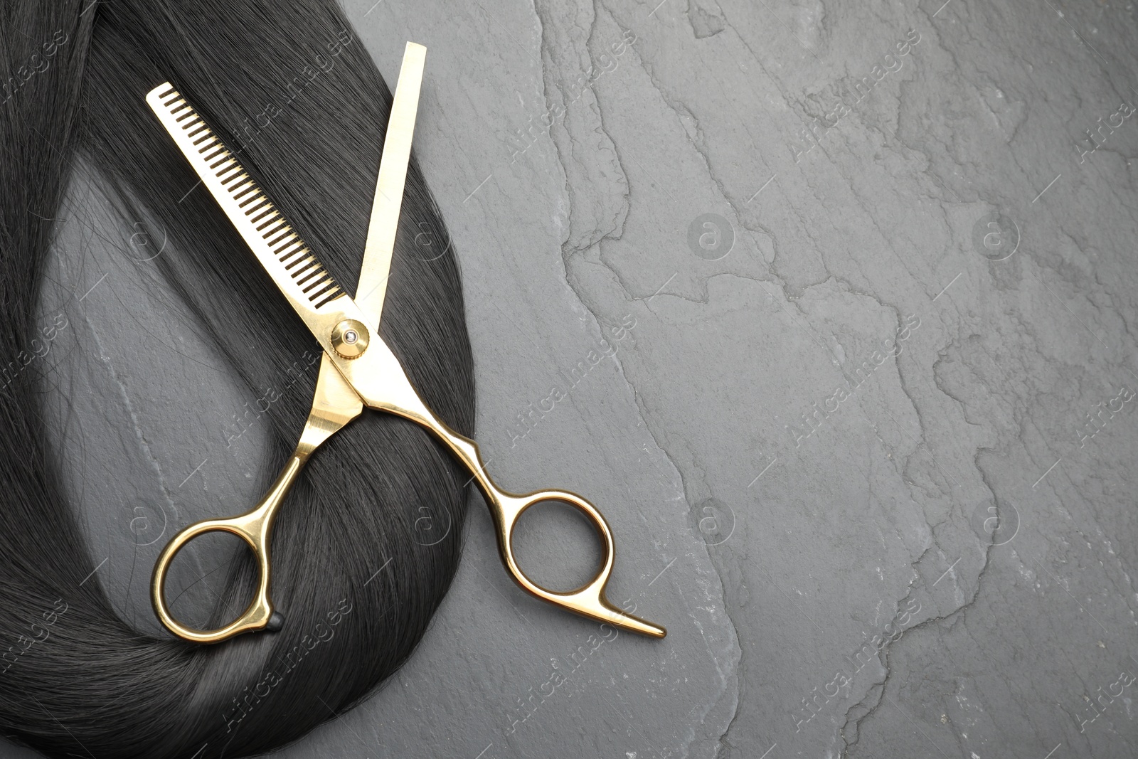 Photo of Black hair strand and professional scissors on grey surface, flat lay. Space for text