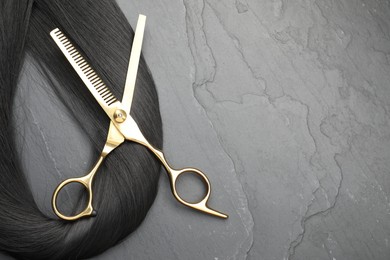 Photo of Black hair strand and professional scissors on grey surface, flat lay. Space for text