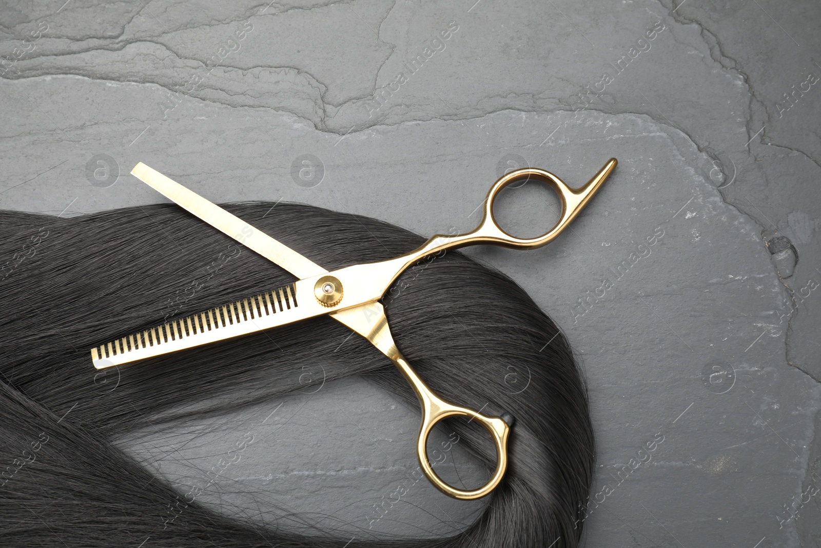 Photo of Black hair strand and professional scissors on grey surface, flat lay