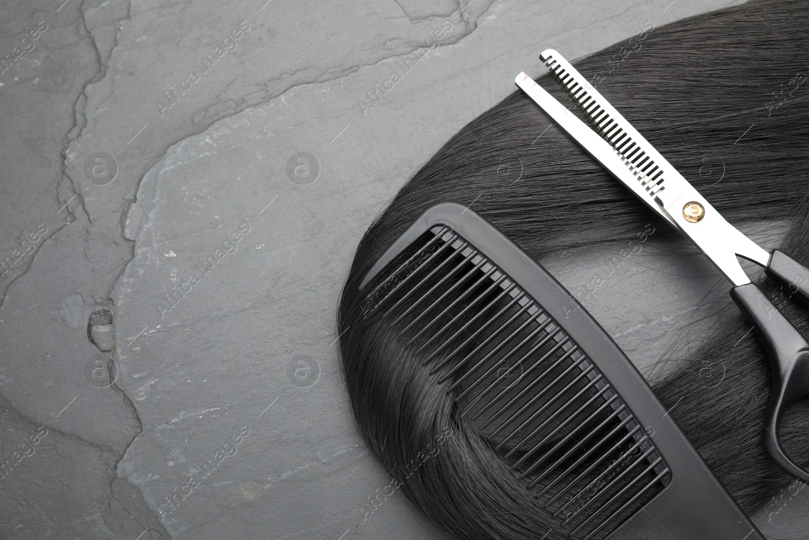 Photo of Black hair strand, comb and professional scissors on grey surface, flat lay. Space for text