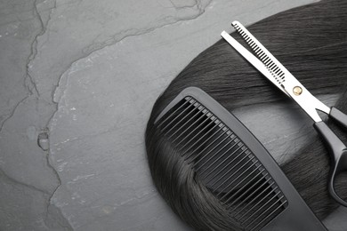 Photo of Black hair strand, comb and professional scissors on grey surface, flat lay. Space for text