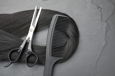 Photo of Black hair strand, comb and professional scissors on grey surface, flat lay