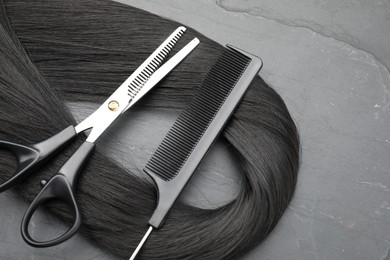 Photo of Black hair strand, comb and professional scissors on grey surface, flat lay