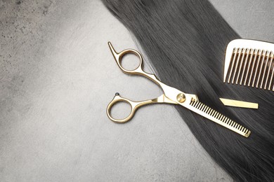 Photo of Black hair strand, comb and professional scissors on grey surface, flat lay. Space for text