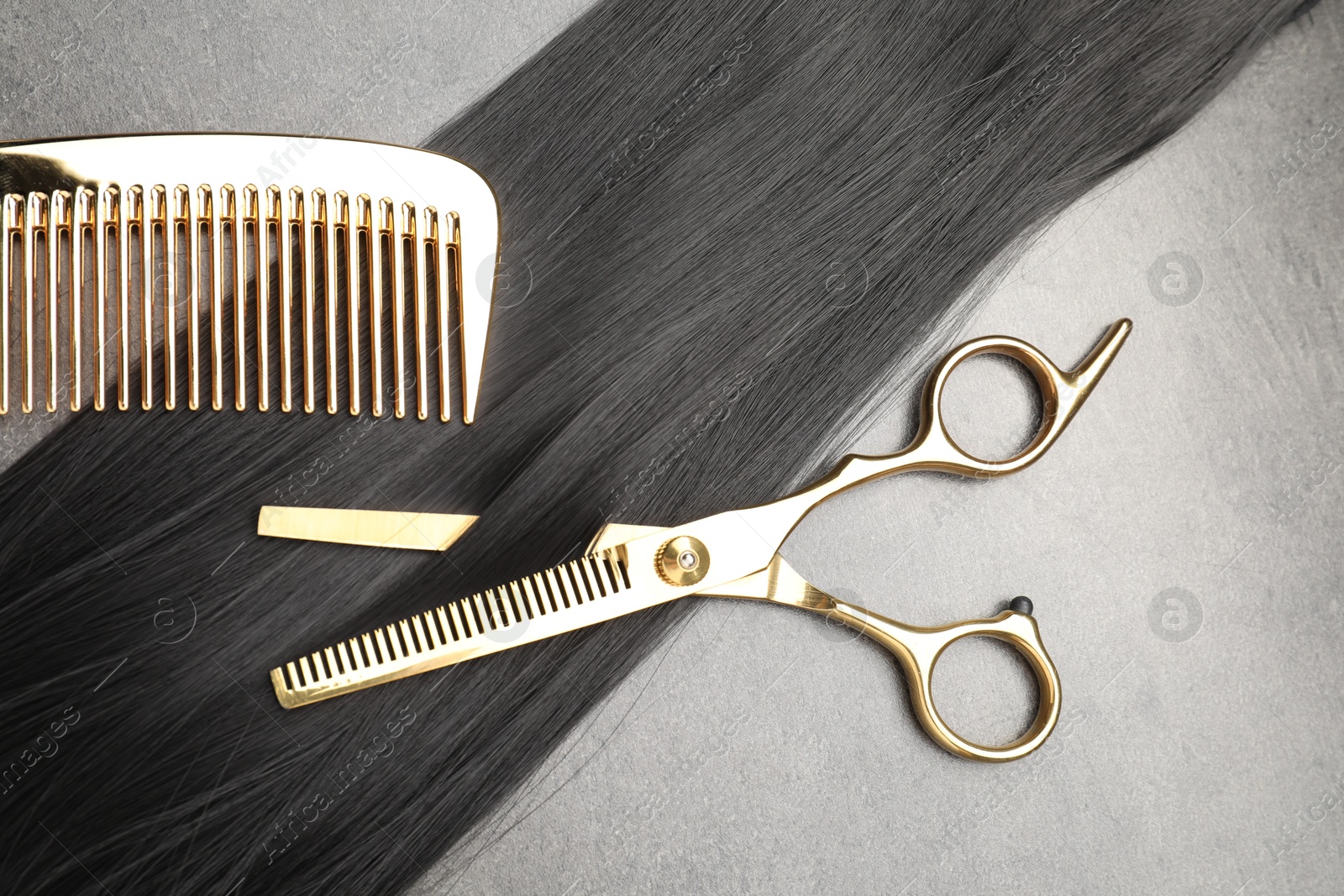 Photo of Black hair strand, comb and professional scissors on grey surface, flat lay